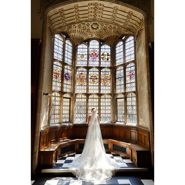 A bride in a wedding dress stands before a large stained glass window in a historic building.