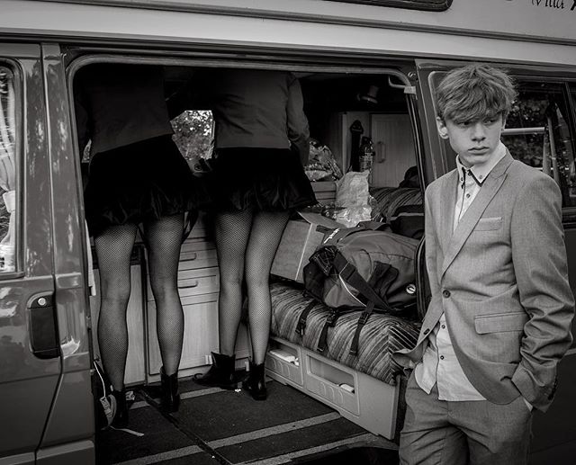 A young man stands outside a van with two figures in fishnet stockings inside. Striking black and white image.