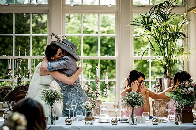 A bride and her mother embrace at a wedding reception, with emotional guests looking on.