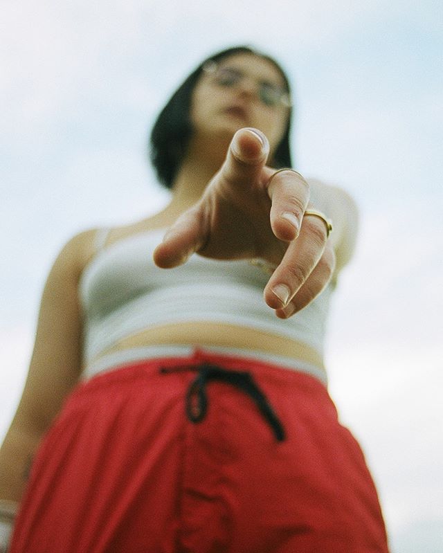 A woman points directly at the viewer with confidence in a low-angle outdoor shot.