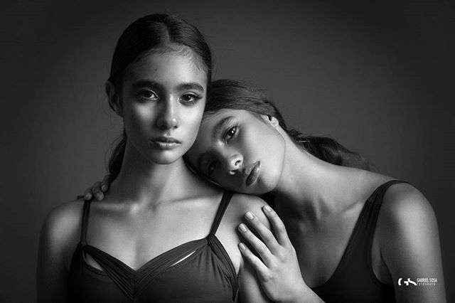 Two beautiful women embrace in a classic black and white studio portrait.