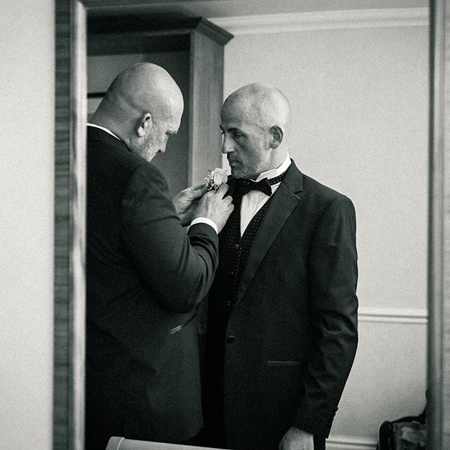 A groom getting ready with assistance on his wedding day, in a classic black and white style.