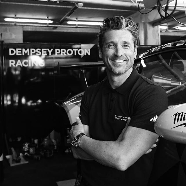 Patrick Dempsey, actor and race car driver, poses in a black and white editorial shot in a garage setting.