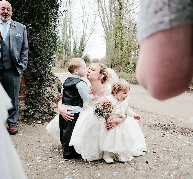 A bride shares a loving moment with children on her wedding day in a candid outdoor shot.