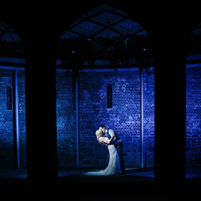 A bride and groom share a romantic kiss under a blue light for their wedding photography.