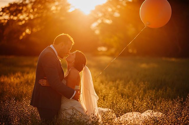 A bride and groom share an intimate moment in a golden field at sunset, holding a balloon during their wedding.