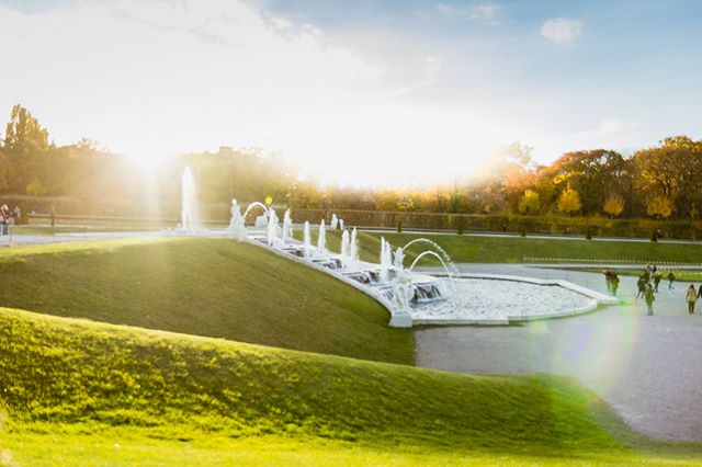 Scenic view of cascading fountains in a lush green park with people walking around.