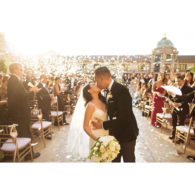 A bride and groom share a kiss during their wedding ceremony as guests celebrate with confetti.