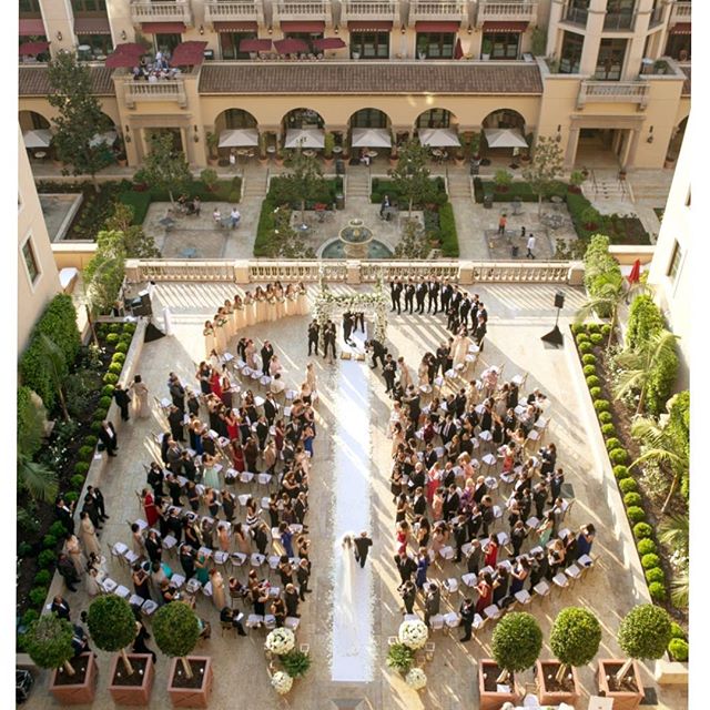An outdoor wedding ceremony with many guests and a clear path, viewed from a high angle.