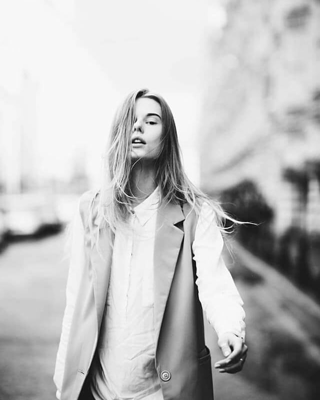 A confident young woman walks down a city street in an editorial fashion style, captured in a striking monochrome shot.