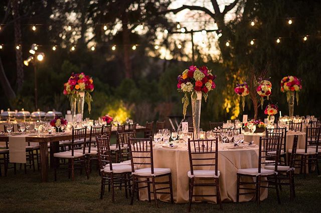 Elegantly decorated tables and chairs are set for an outdoor wedding reception under twinkling string lights.