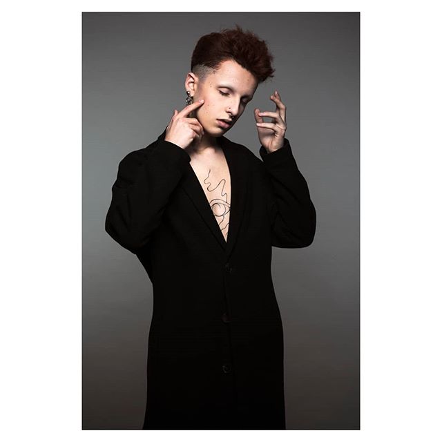 A stylish man in a black coat poses with his tattoo showing.