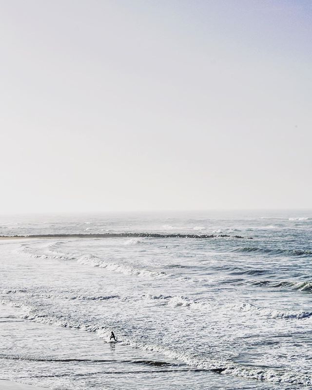 A lone surfer catches a wave in a calm ocean under a bright, hazy sky, creating a serene coastal scene.