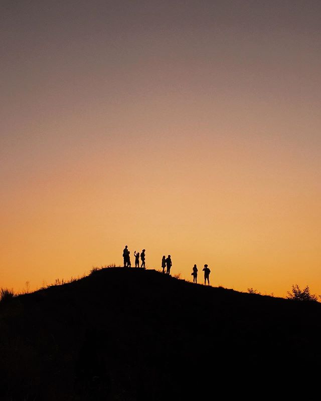 A silhouette of a group of people standing on a hill against a vibrant sunset sky.