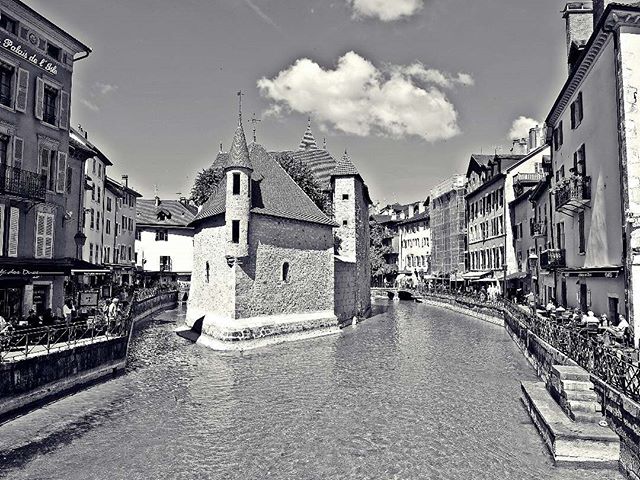 The historic Palais de l'Isle in Annecy, France, surrounded by canals on a sunny day in black and white.