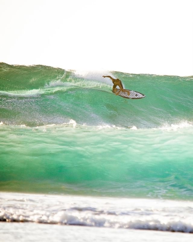 A surfer rides a turquoise wave on a sunny day, capturing the energy of the sport and beach lifestyle.