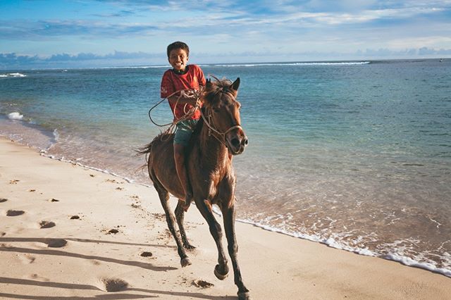 A cheerful boy enjoys a horseback ride on a beautiful beach, with the ocean waves gently rolling in the background.