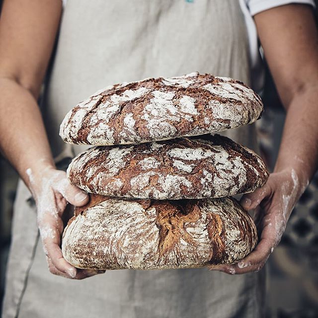 A stack of freshly baked sourdough bread loaves held by a baker, showcasing rustic and artisanal quality.