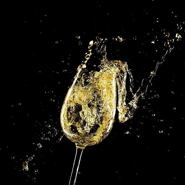 A glass of white wine mid-splash against a stark black backdrop, capturing the essence of a lively celebration.