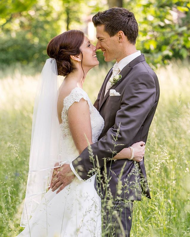 A bride and groom embrace in a field, noses touching, on their wedding day.