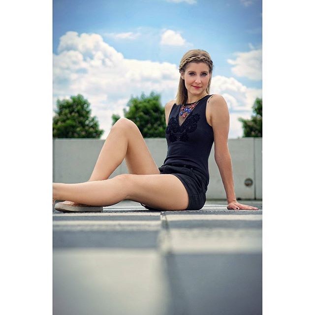 A brunette woman sits on a rooftop with a relaxed expression, enjoying the outdoor ambiance.