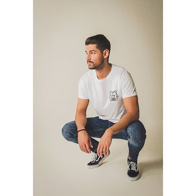 A stylish man in a white t-shirt and jeans poses in a studio.