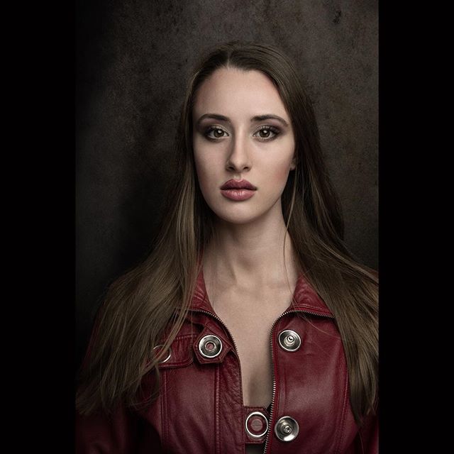 Portrait of a brunette woman in a red leather jacket with a serious expression.