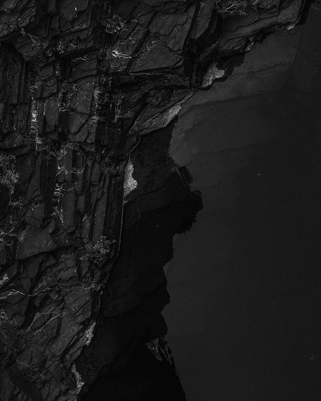 A dramatic monochrome image of a rocky cliff face on the coast, conveying mystery and natural intensity.