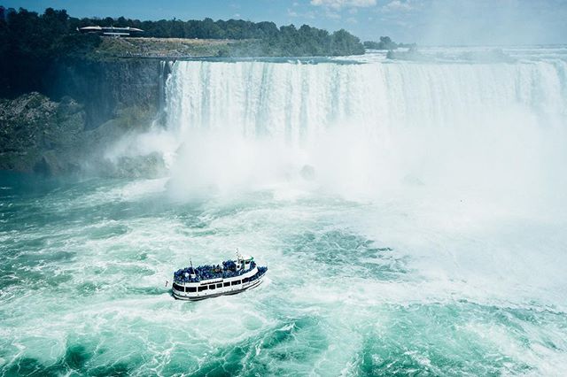 A tour boat navigates the turbulent waters below Niagara Falls, enveloped by mist and cascading water.