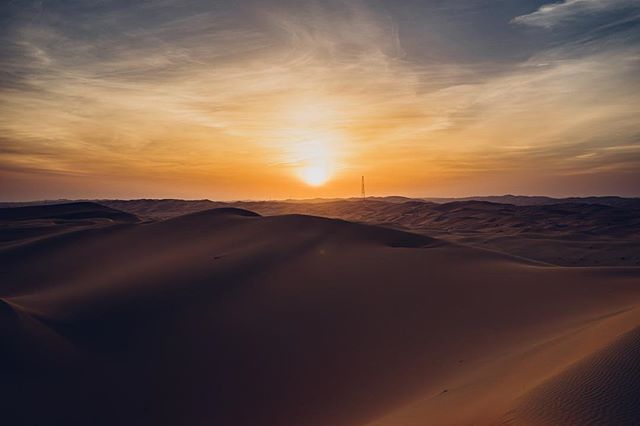 A scenic desert landscape with rolling sand dunes and a vibrant sunset illuminating the horizon.