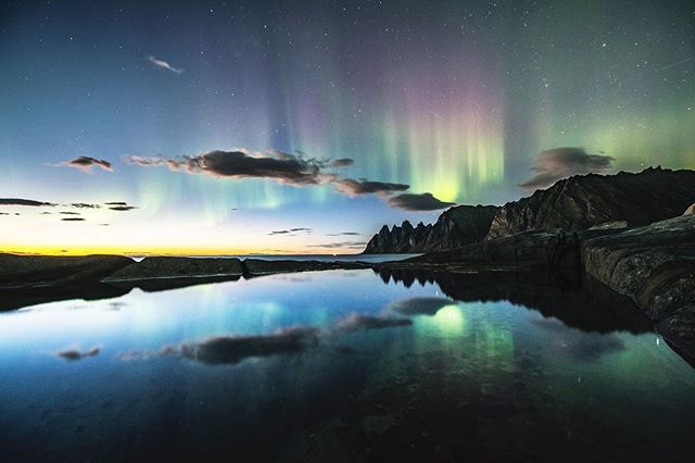 A stunning aurora borealis lights up the night sky over mountains reflected in the tranquil waters of Norway.