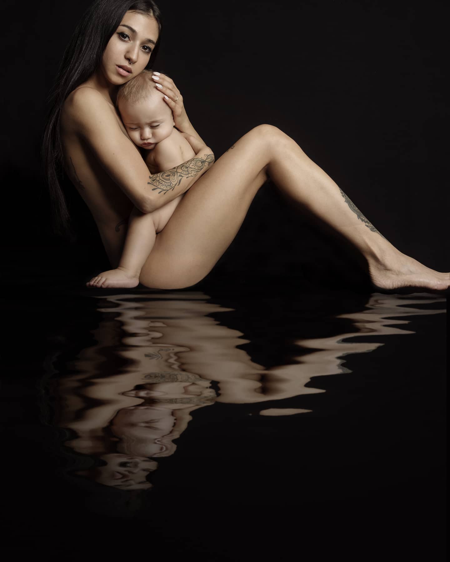 A nude woman is tenderly holding a baby in a studio setting, artistic and emotional.