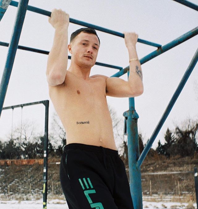 A shirtless man does pull-ups on a blue bar in a snowy outdoor setting, showcasing fitness and strength.