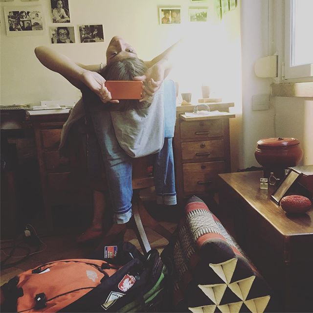 A person takes a selfie in a room with furniture, decor, and a backpack on the floor.