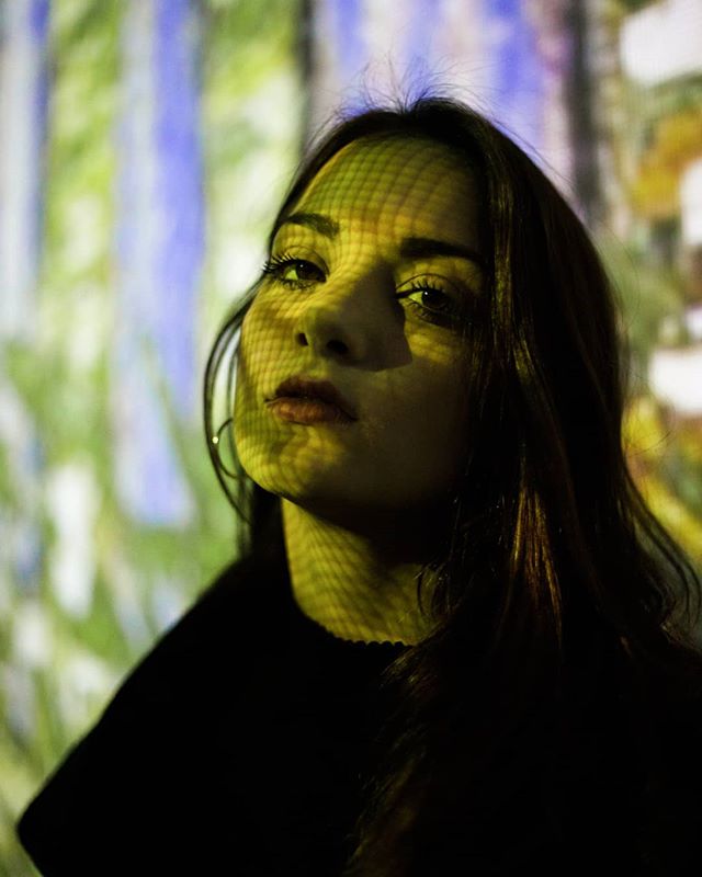A woman with long dark hair poses in front of a colorful, abstract background projection for a fashion editorial.