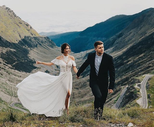 A happy wedding couple walks hand-in-hand through the mountains on their wedding day.