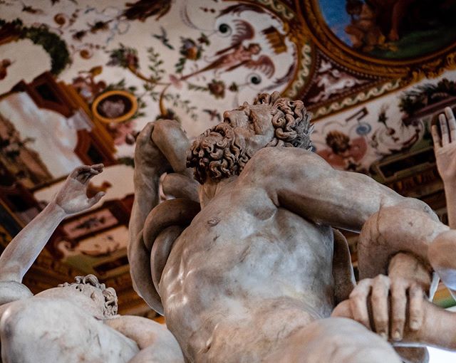 An image shows a marble statue of two men wrestling, evoking classical art, historical sculpture, and indoor display.