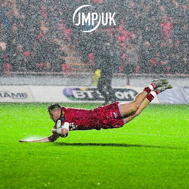 A rugby player dives to score a try in the rain during a match, showcasing athleticism and determination.