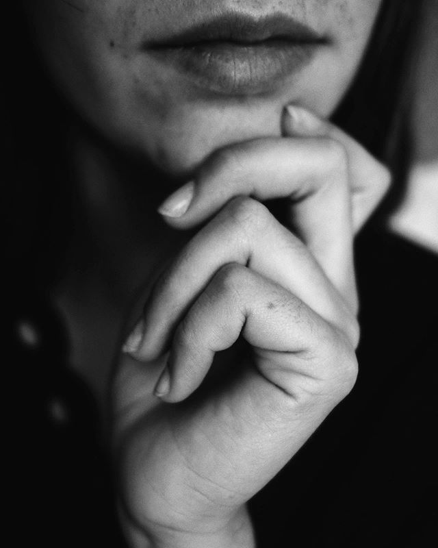 A contemplative black and white image showing a woman's face with her hand resting on her chin in a thoughtful pose.