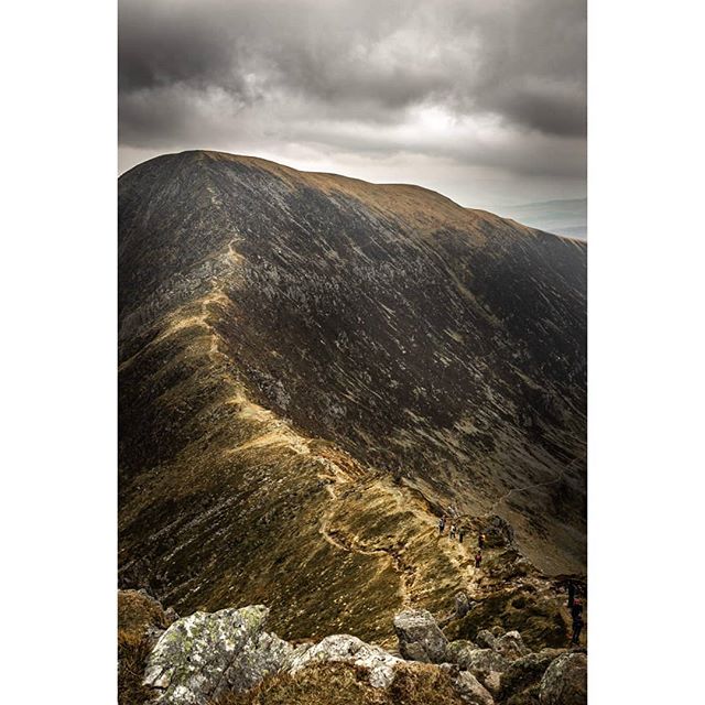 A scenic mountain ridge with a trail and hikers under a dramatic sky, inspiring outdoor adventure and tourism.