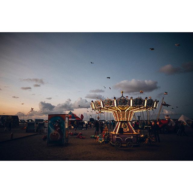 A lively fairground scene with a lit carousel and a crowd enjoying the evening atmosphere.
