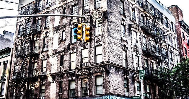 A vintage-style building with fire escapes and a traffic light at a corner in an urban setting.