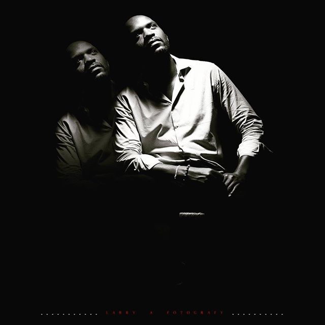 A black and white portrait of a man in a shirt, with dramatic lighting and a reflective double exposure.