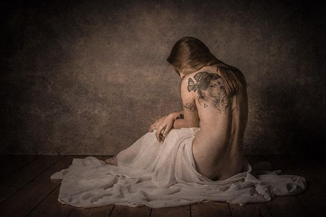 Artistic nude shot of a woman with a tattoo on her back, evoking intimacy and contemplation.