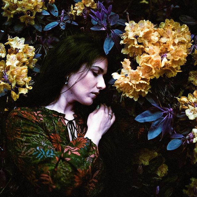 A woman peacefully rests amidst yellow flowers, creating a serene and intimate portrait perfect for editorial or social media.