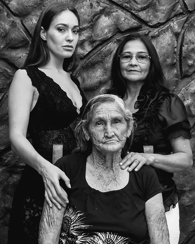 A black and white portrait of three generations of women - daughter, mother, and grandmother - standing closely together.