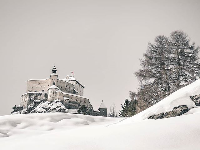 A snow-covered castle sits atop a hill amidst a serene winter landscape. A historical and scenic location. 