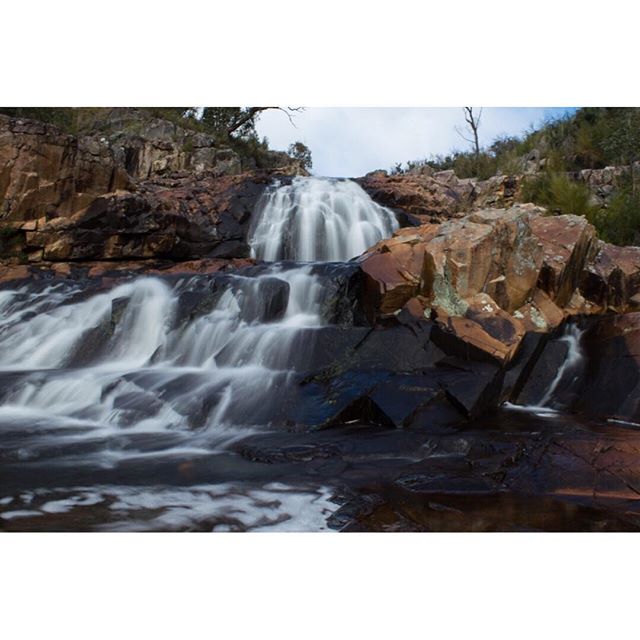 A scenic waterfall cascading over rocks in a natural outdoor setting, perfect for travel or nature backgrounds.
