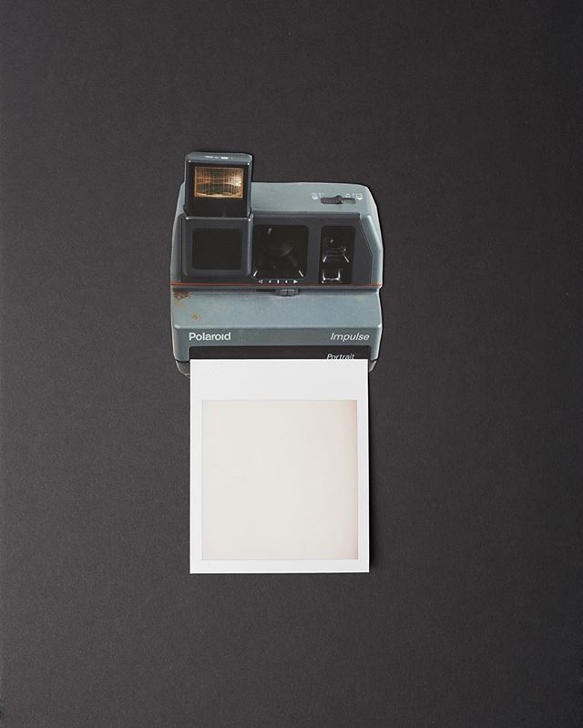 An impulse portrait polaroid camera with a blank instant film photo on a black background.