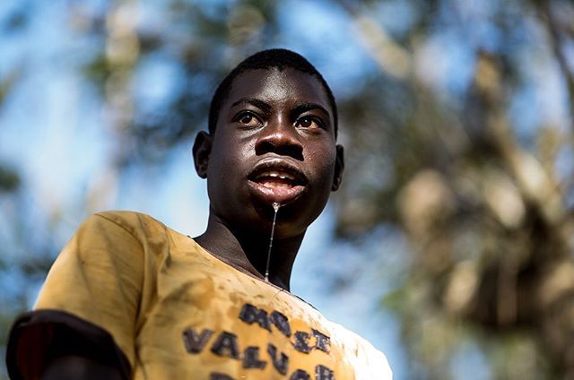 A young boy looks up with water dripping from his face, wearing a yellow shirt.